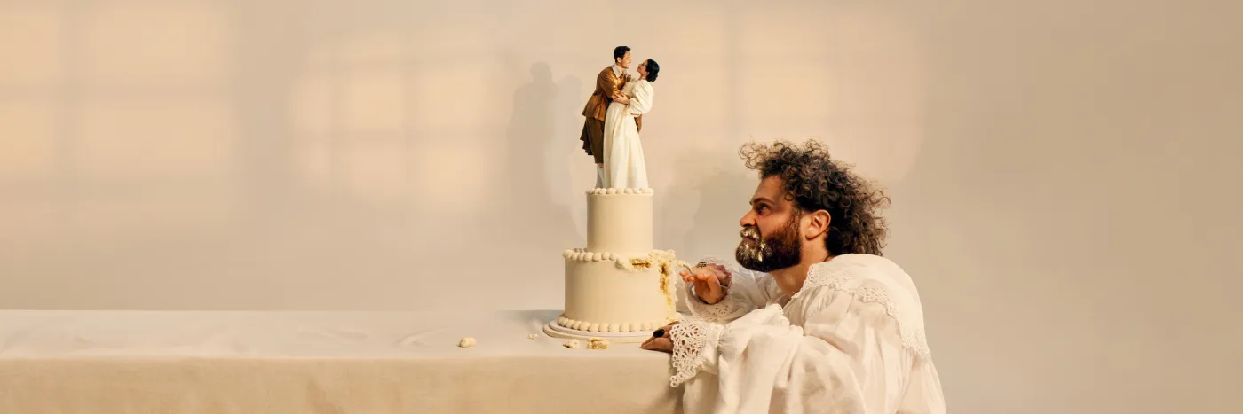 A bearded man picks away and glares at a wedding cake with a happy couple in period costume at the top.