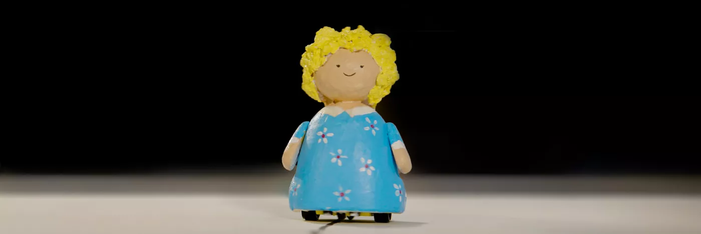 A small doll with blonde hair smiles. She wears a blue dress.