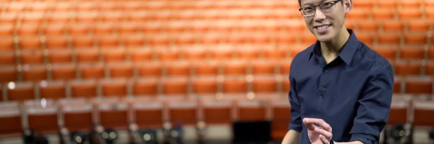 A man in a blue shirt standing in front of an empty theatre.