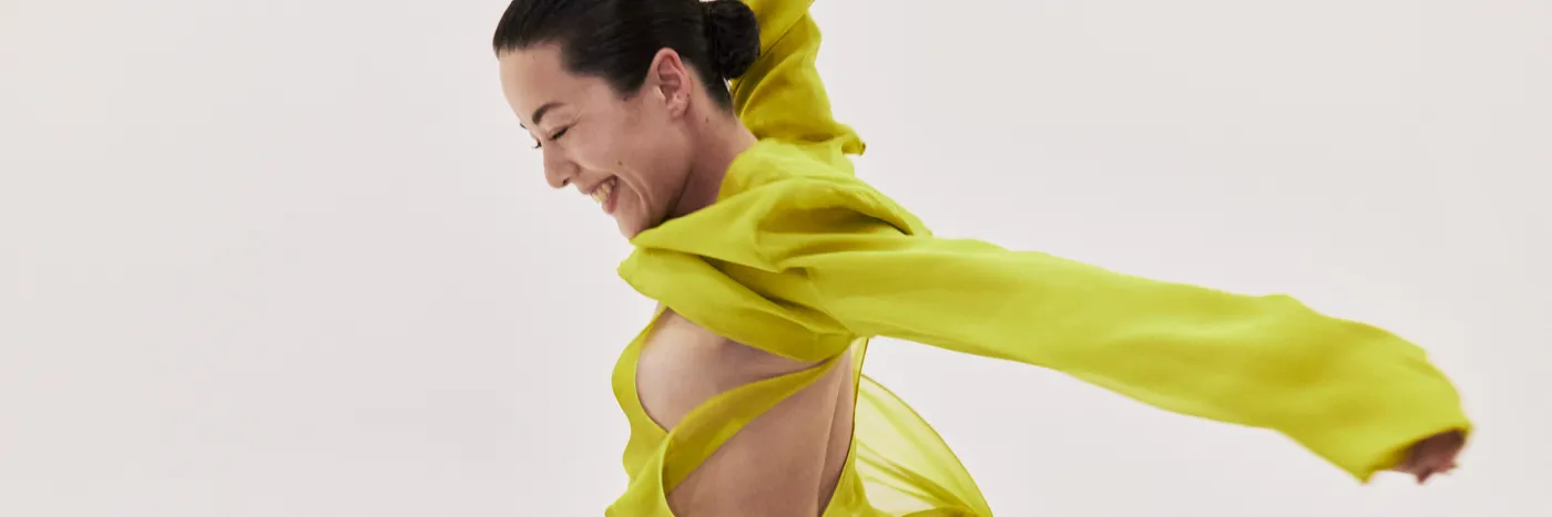A dancer in bright yellow, in motion against a light grey background.