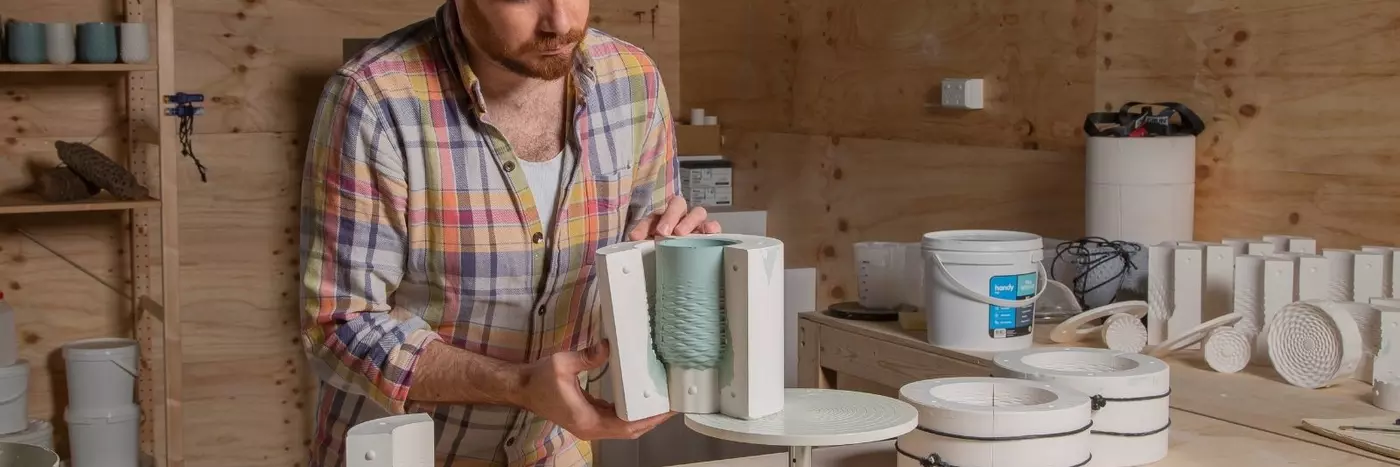 A man in a shirt crafting a blue object in a wooden room.