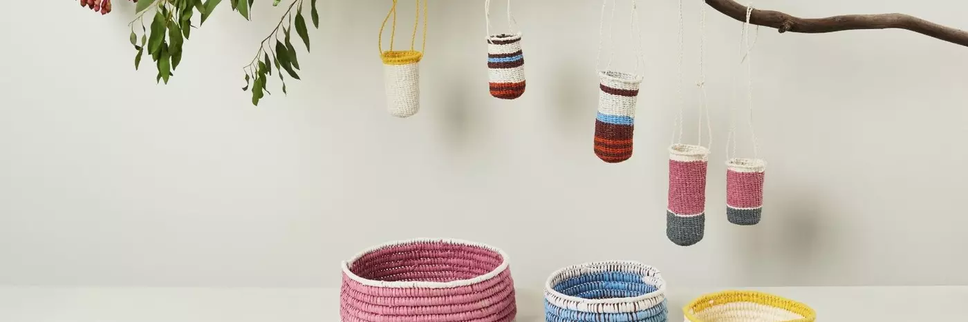 Five knitted buckets hanging off a branch underneath three colored bowls.