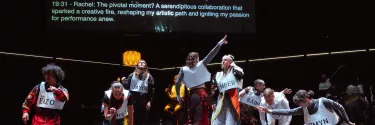 A diverse group of individuals stands on stage, dancing in front of a large projector screen displaying AI-generated text as movement suggestions.